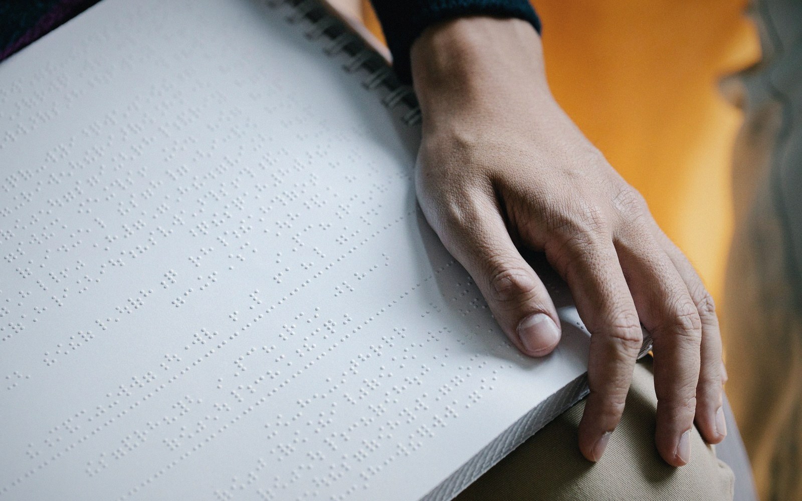 A hand resting on a page of raised braille text in a spiral-bound book