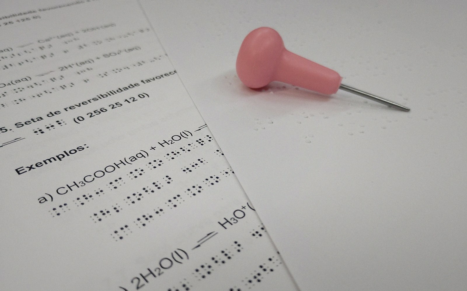 A braille chemistry worksheet lies beside a stylus with a pink handle