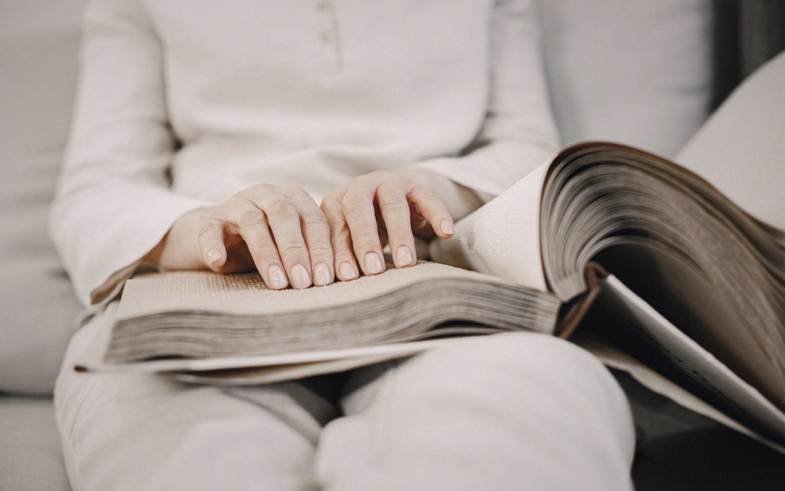 Hands resting on the open pages of a thick book in someone's lap