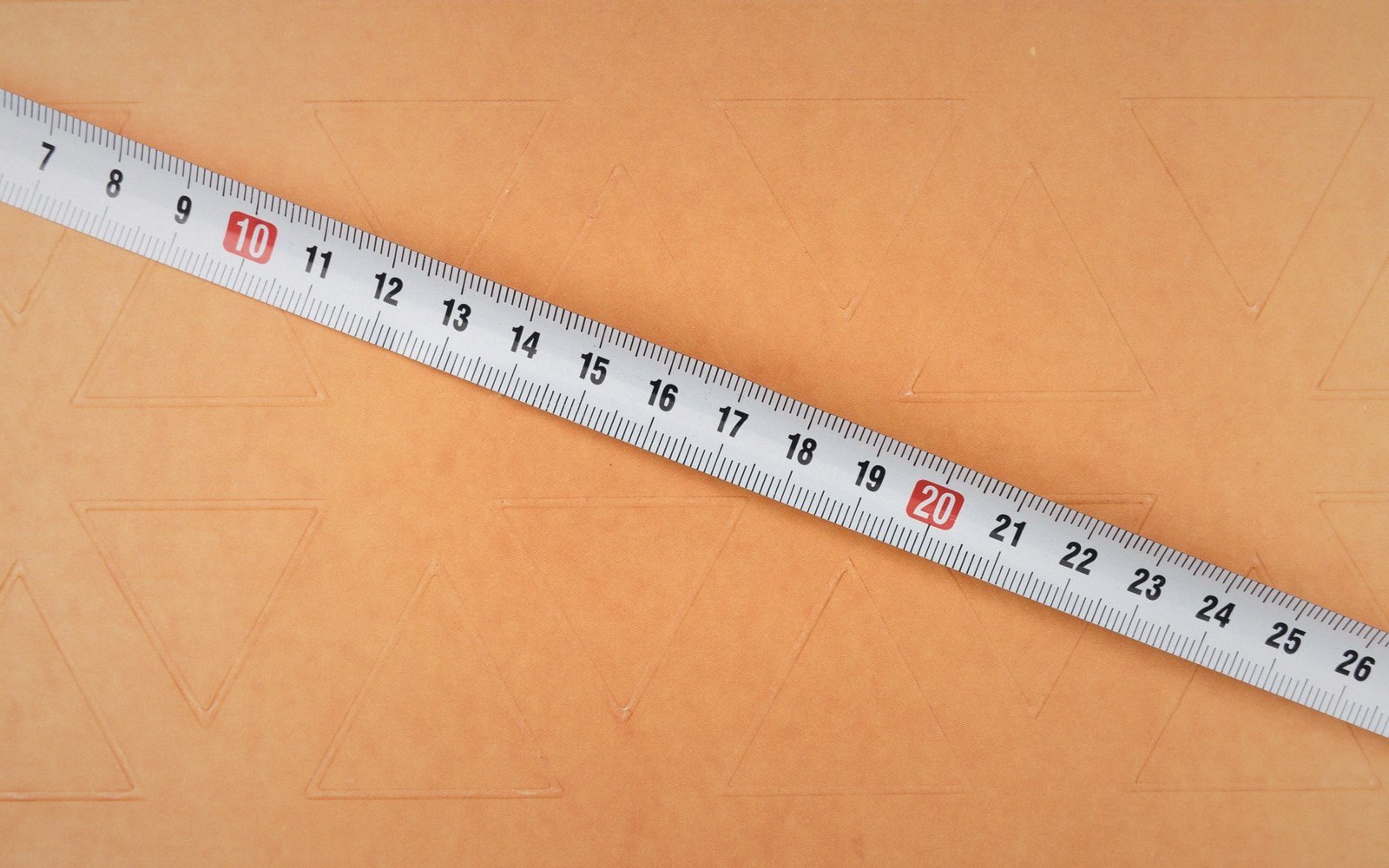 A metal tape measure lying diagonally across a tan surface with faint triangle patterns
